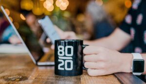 A man holding a black mug with 80/20 print browsing his laptop and searching on how to make his email deliverability rate accurate